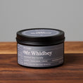 Load image into Gallery viewer, Mr. Whidbey scented soy candle in black metal tin on wooden surface.