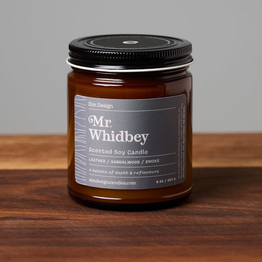 Mr. Whidbey scented soy candle in amber glass jar on wooden surface.