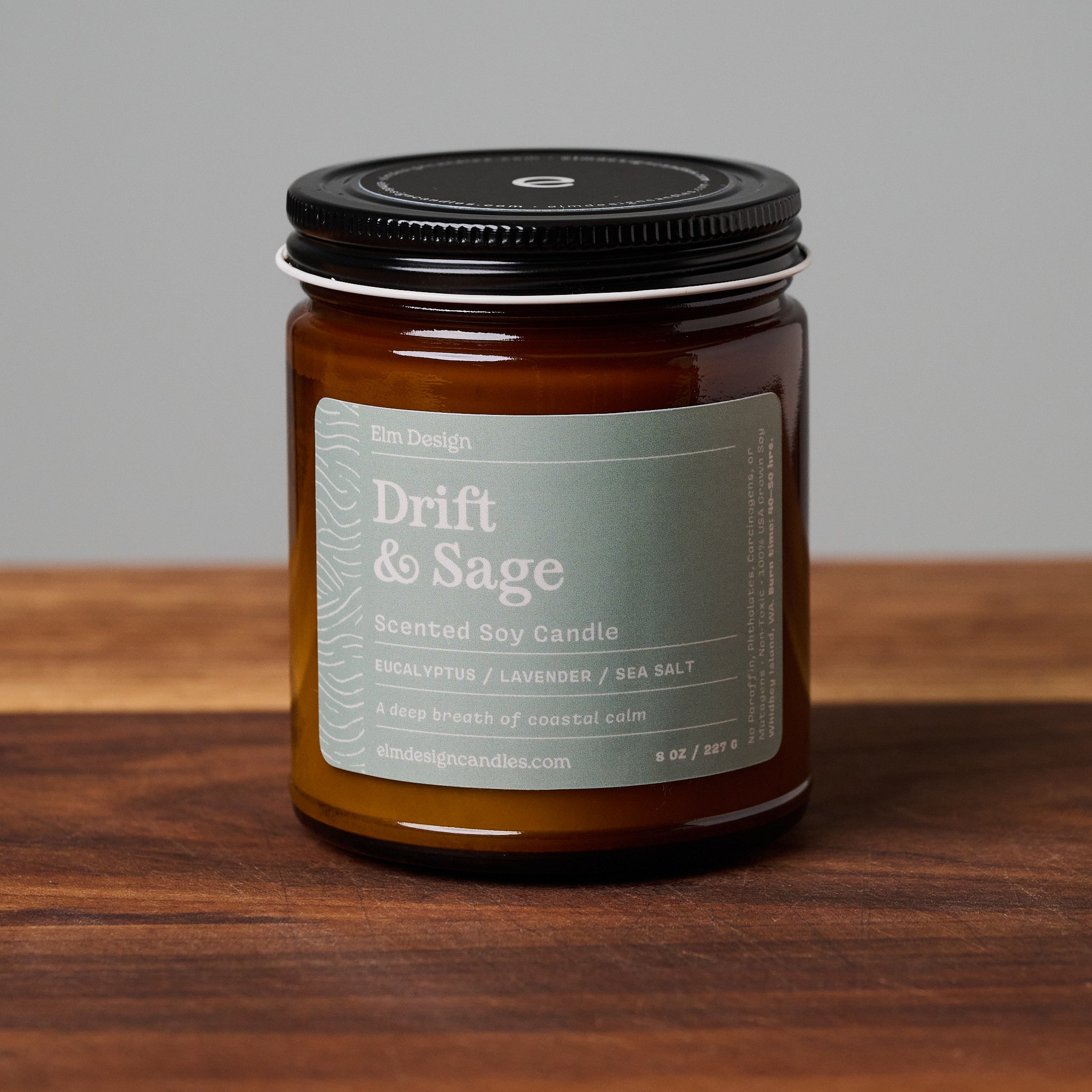 Drift & Sage scented soy candle in amber glass jar on wooden surface.