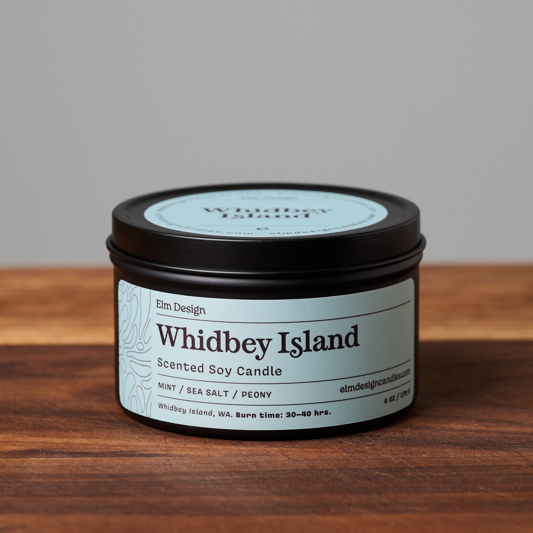 Whidbey Island scented soy candle in black metal tin on wooden surface.
