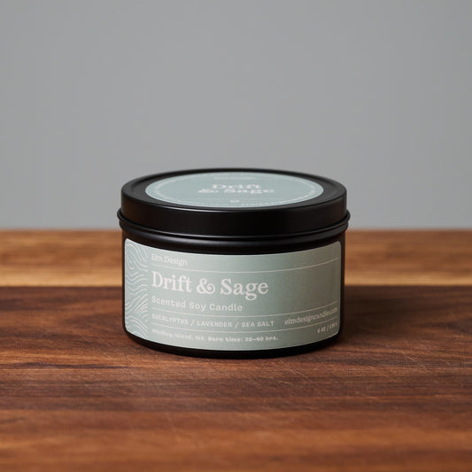 Drift & Sage scented soy candle in black metal tin on wooden surface.
