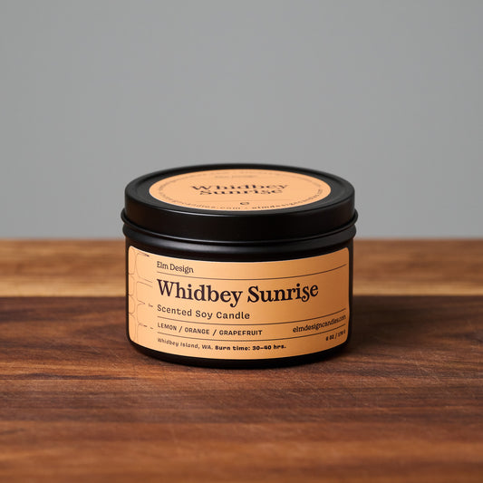 Whidbey Sunrise scented soy candle in black metal tin on wooden surface.