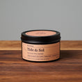 Load image into Gallery viewer, Tide & Sol scented soy candle in black metal tin on wooden surface.
