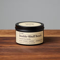 Load image into Gallery viewer, Double Bluff Beach scented soy candle in black metal tin on wooden surface.
