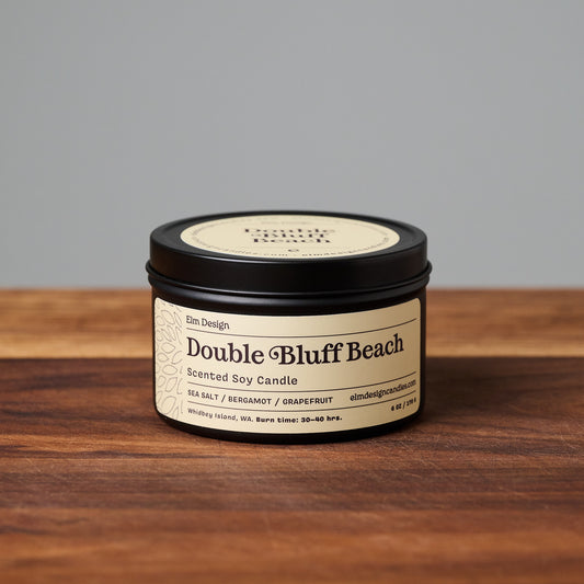 Double Bluff Beach scented soy candle in black metal tin on wooden surface.