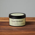 Load image into Gallery viewer, Island Weekend scented soy candle in black metal tin on wooden surface.
