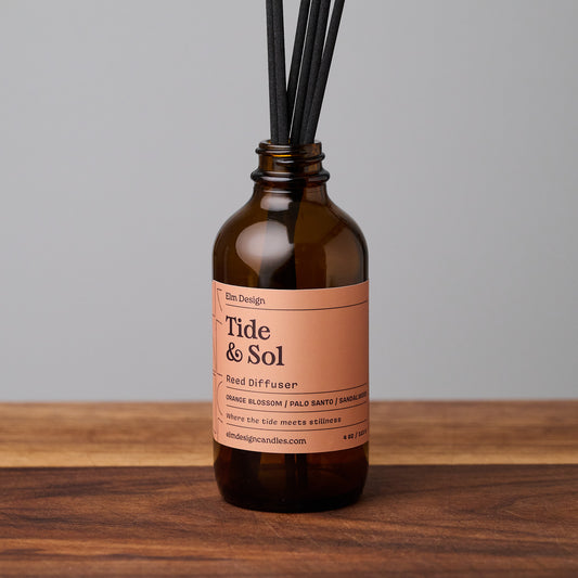 Tide & Sol scented reed diffuser in amber glass jar with black reeds on wooden surface.