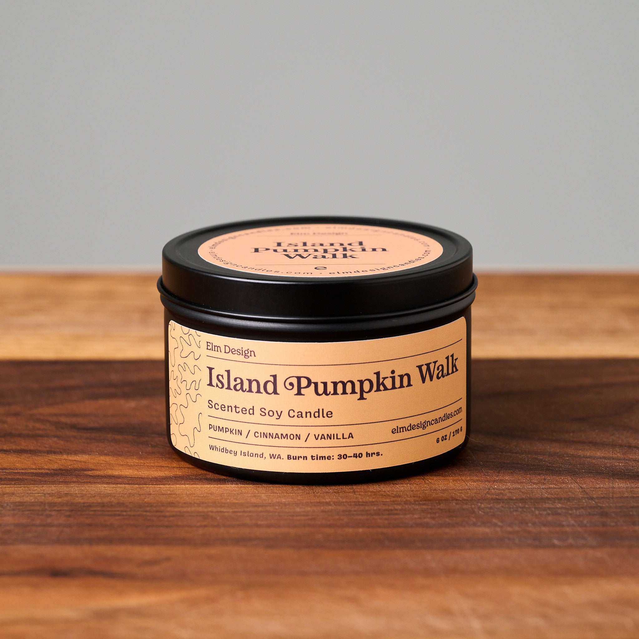 Island Pumpkin Walk scented soy candle in a 6oz matte metal tin placed on a wooden cutting board with a light gray background.