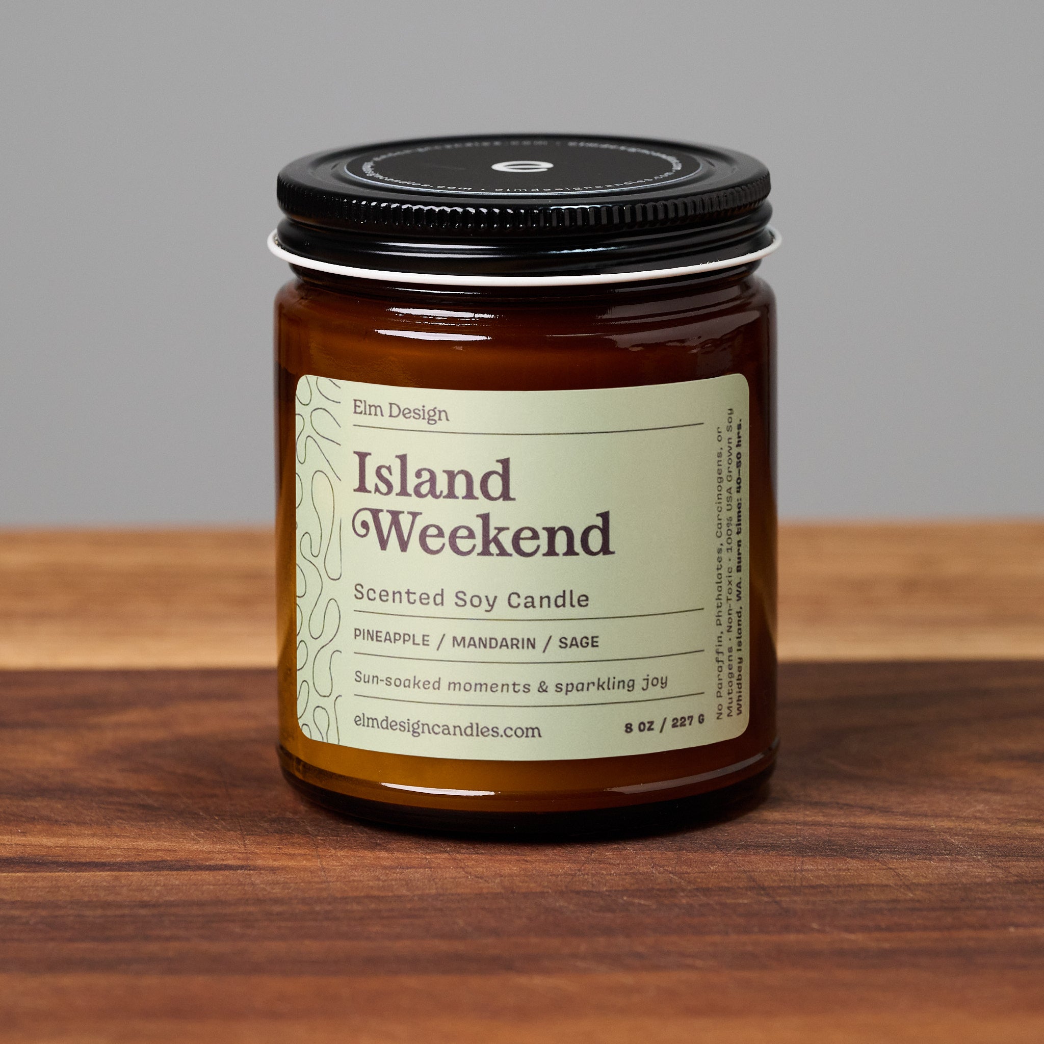 Island Weekend scented soy candle in amber glass jar on wooden surface.