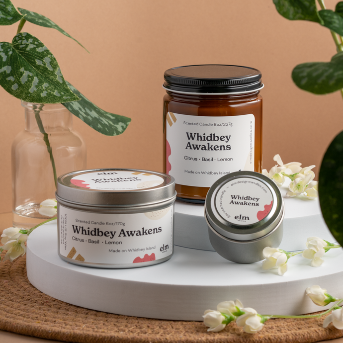 Whidbey Awakens scented soy candles in colorfully labeled 8, 6 and 2 oz containers.